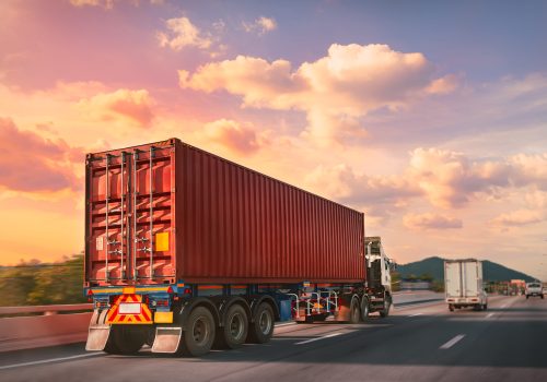 Truck with red container on the highway with sunset time, logistic import export and transport industry concept.